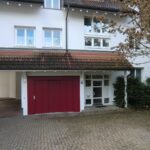 Außenansicht eines Hauses mit rotem Garagentor und Eingang