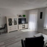 Helles Wohnzimmer mit großem Fenster, eleganter Vitrine, Fernseher und gemütlicher Sitzecke in einer Ferienwohnung in Küssaberg.