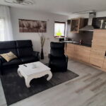 Gemütliches Wohnzimmer mit moderner Küche in einer Ferienwohnung in Küssaberg. Schwarze Ledersessel, weißer Couchtisch, und helle Holzküche mit Einbaugeräten.