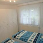 Schlafzimmer in der Ferienwohnung Ahorn mit zwei Einzelbetten, einem modernen Kleiderschrank und einer gemütlichen Bettdecke im blauen Design. Helle Farben und viel Tageslicht sorgen für eine angenehme Atmosphäre.