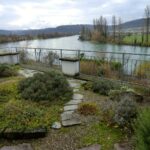 Gartenbereich mit Kiesweg und Pflanzen, der auf den Fluss hinausblickt