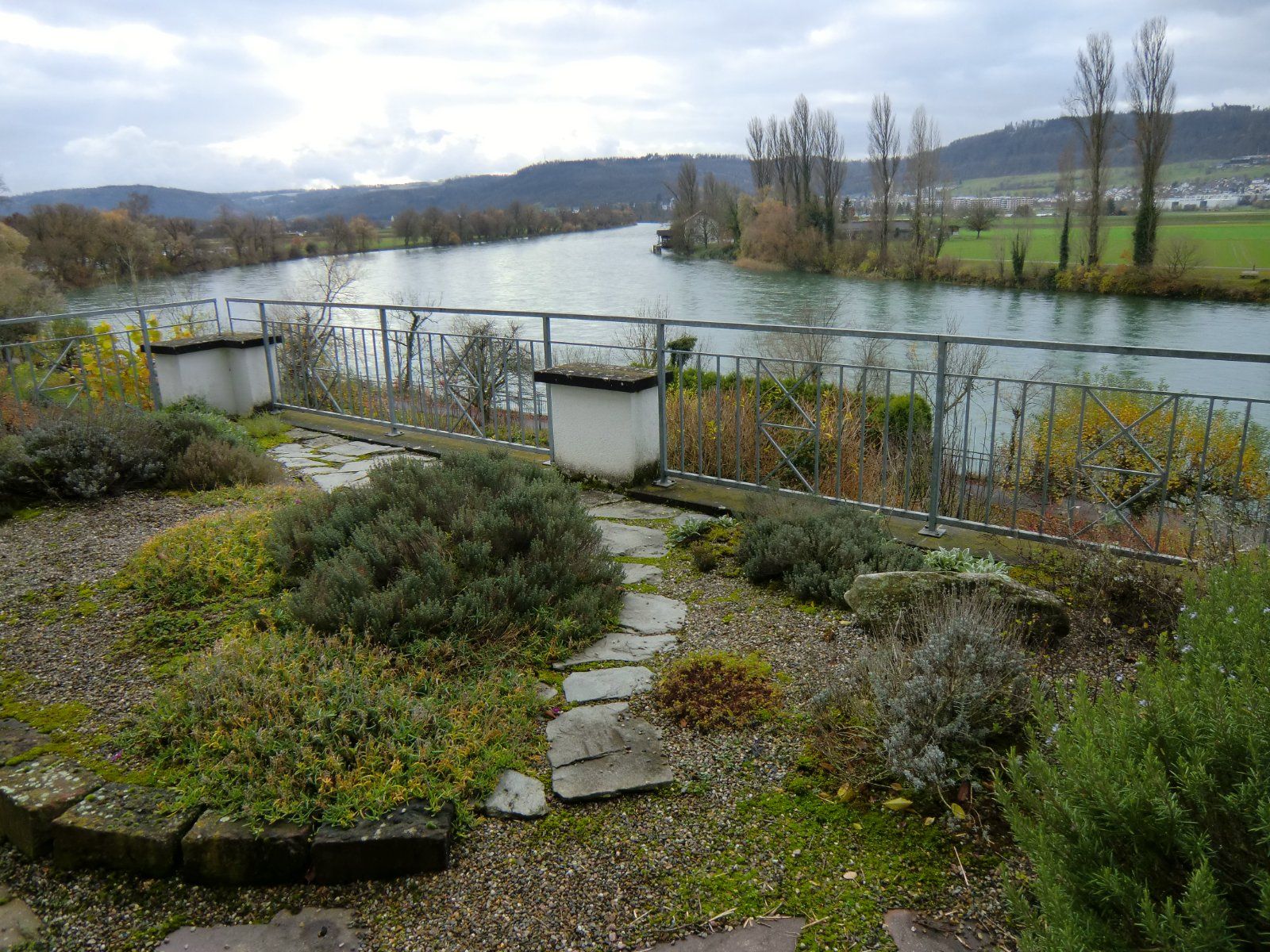 Gartenbereich mit Kiesweg und Pflanzen, der auf den Fluss hinausblickt