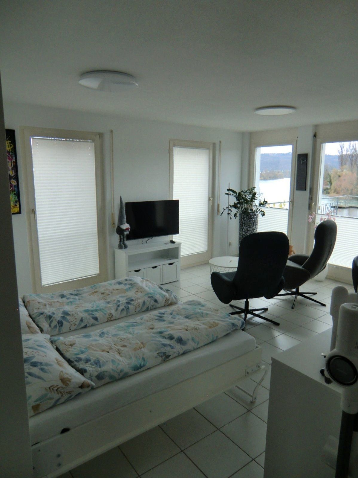 Modernes Schlafzimmer mit Doppelbett und Sitzgruppe neben großen Fenstern