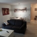 Wohn- und Essbereich der Ferienwohnung mit Sofa, Esstisch und dekorativen Bildern