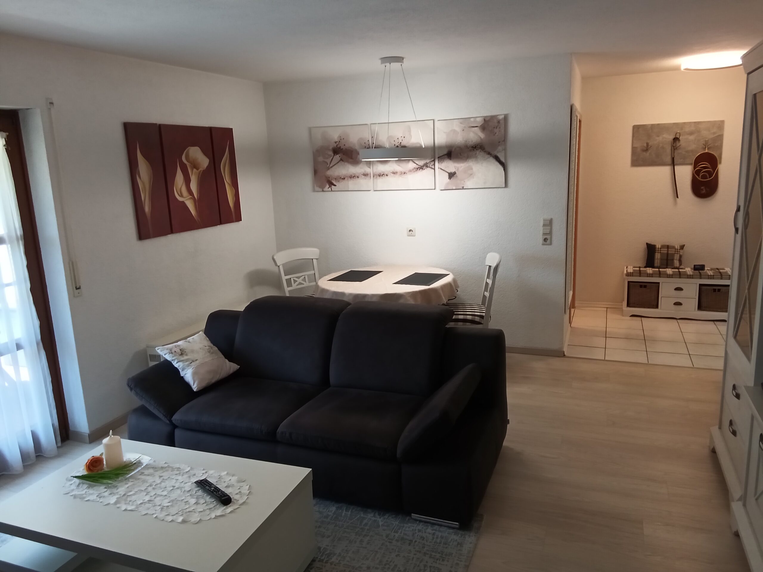 Wohn- und Essbereich der Ferienwohnung mit Sofa, Esstisch und dekorativen Bildern