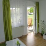 Wohnzimmer der Ferienwohnung mit Zugang zur Terrasse und grünen Vorhängen