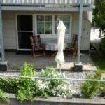 Die Terrasse der Ferienwohnung Ahorn mit Gartenmöbeln und einem Sonnenschirm, umgeben von Pflanzen und Blumen, bietet einen idealen Platz zum Entspannen im Freien.