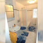 Modernes Badezimmer in der Ferienwohnung Ahorn mit Dusche, Waschbecken und WC. Blaue Badteppiche und ein großes Fenster sorgen für eine helle und freundliche Atmosphäre