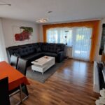 Offenes Wohnzimmer mit Esstisch und gemütlicher Eckcouch in der Ferienwohnung Ahorn. Die großzügige Fensterfront bietet einen schönen Ausblick und viel Tageslicht.