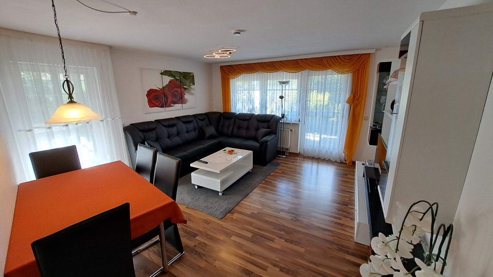 Offenes Wohnzimmer mit Esstisch und gemütlicher Eckcouch in der Ferienwohnung Ahorn. Die großzügige Fensterfront bietet einen schönen Ausblick und viel Tageslicht.